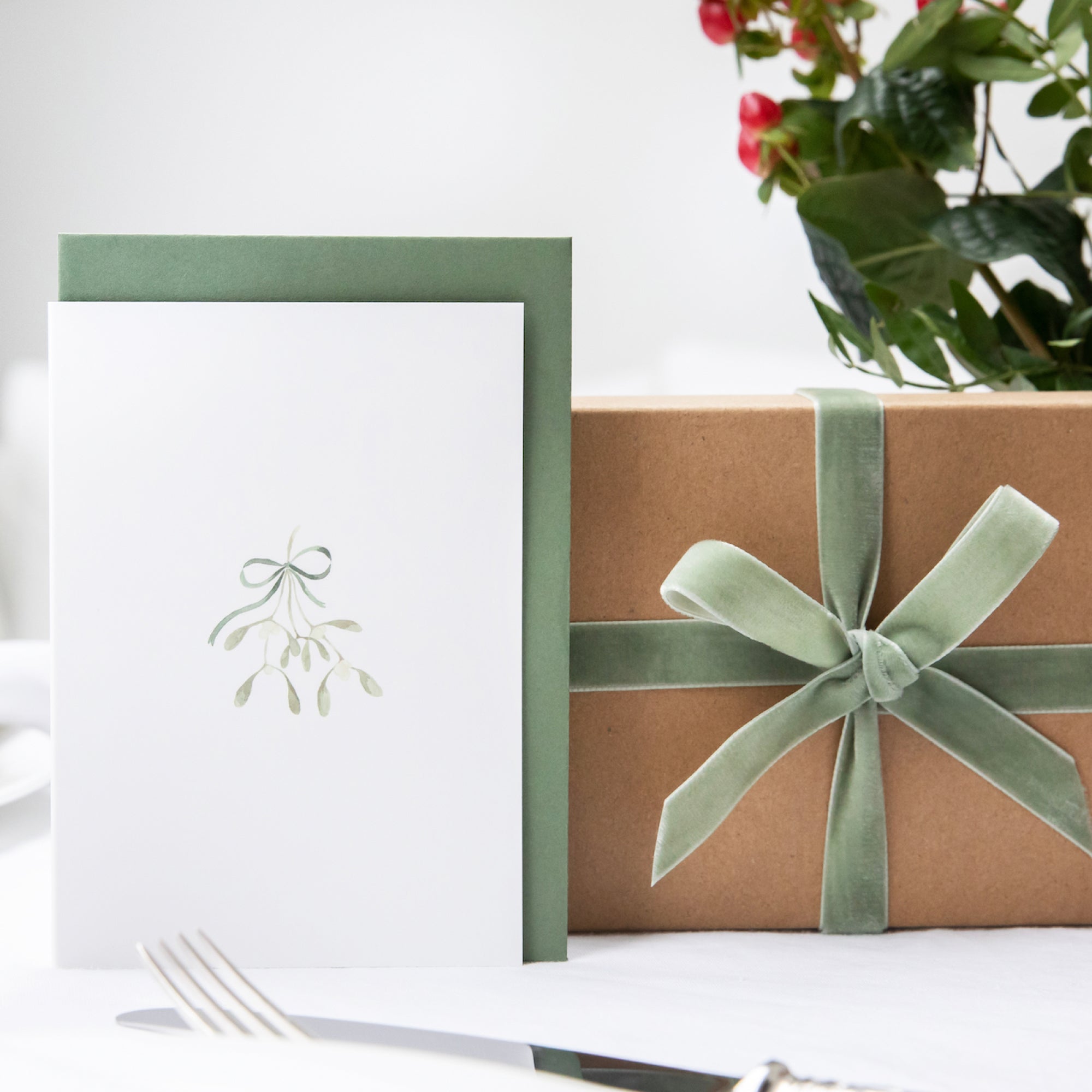 Luxury Christmas Card by Memo Press with a watercolour illustration of mistletoe tied with a ribbon tied with a bow and comes with a green envelope made in Britain