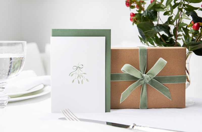 Luxury Christmas Card by Memo Press with a watercolour illustration of mistletoe tied with a ribbon tied with a bow and comes with a green envelope made in Britain